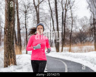 Hiver running sport femme portant une veste et une montre intelligente. Faites du jogging asiatique dans la forêt d'hiver en faisant de l'exercice de course en extérieur. Mode de vie actif. Banque D'Images
