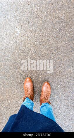 Vue de dessus selfie des pieds de femme en bottes d'automne brunes sur asphalte humide après la pluie. Banque D'Images