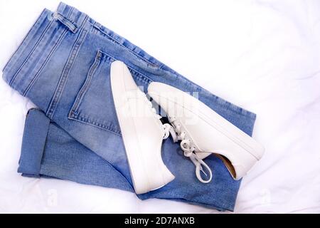 Concept de mode minimaliste. Baskets et jeans tendance sur fond textile. Vue de dessus Banque D'Images