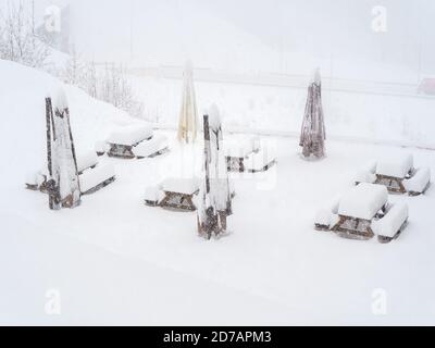 Des tables enneigées avec des bancs et des parasols d'extérieur pliés sont installés le site pendant une journée d'hiver pendant un blizzard Banque D'Images