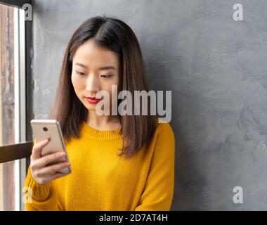 Jeune femme asiatique sérieuse et réfléchie regardant le téléphone mobile, lisant des messages Banque D'Images