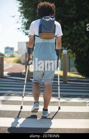une personne handicapée sur des béquilles traverse la route Banque D'Images
