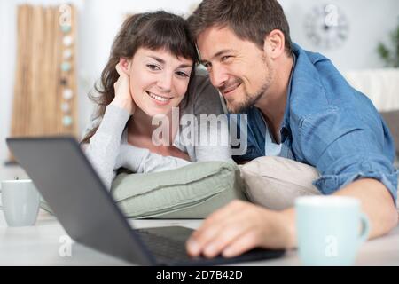 couple accrocheuillé sur des coussins regardant l'ordinateur portable Banque D'Images