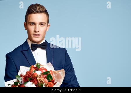 homme romantique avec un bouquet de fleurs et dans un noeud papillon sur fond bleu vue rognée Banque D'Images