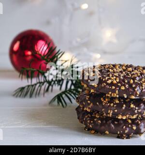 L'arrivée et l'ambiance de Noël, Elisenlebkuchen avec glaçage au chocolat et noisettes, sur une table en bois blanc à l'arrière-plan une boule de noël rouge Banque D'Images