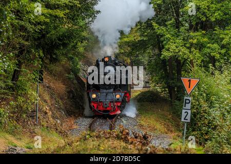 Vue de face d'une locomotive à vapeur sous la vapeur dans une vallée des monts Harz. Chemin de fer étroit avec wagon dans les montagnes avec arbres et roc f Banque D'Images