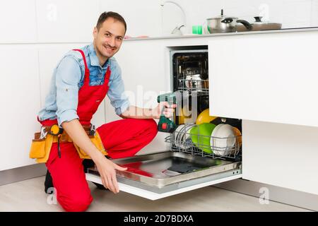 Homme technicien assis près du lave-vaisselle dans la cuisine Banque D'Images