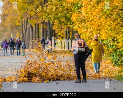 Moscou. Russie. 11 octobre 2020 : une employée de services publics utilise un souffleur pour enlever les feuilles tombées dans une allée d'un parc. Les feuilles jaunes volent dans le Banque D'Images