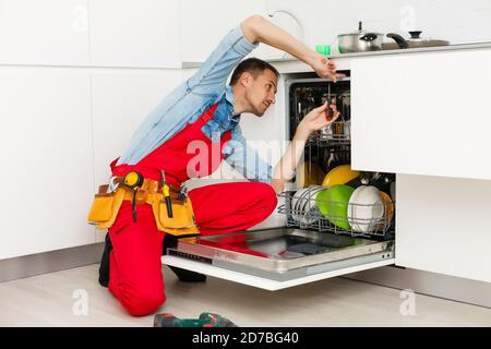 Homme technicien assis près du lave-vaisselle dans la cuisine Banque D'Images