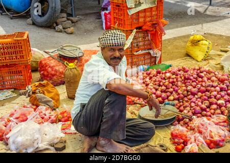 Détenteur de la pile assis dans un stand vendant des produits locaux, des oignons et des tomates, dans un marché en bord de route dans un village de Madhya Pradesh, en Inde Banque D'Images