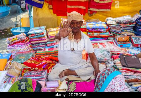 Sympathique et souriant, il est assis dans une cabine qui vend des tissus colorés sur un marché en bord de route dans un village de Madhya Pradesh, en Inde Banque D'Images