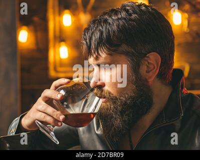 L'homme boit du brandy ou du whisky. Homme barbu portant une veste et buvant du whisky ou du cognac. Homme sérieux ayant la dépendance à l'alcool et à la nicotine Banque D'Images