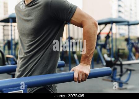 Gros plan du muscle d'un jeune homme qui fait des creux sur des barres irrégulières à l'extérieur. Introduction au sport et à un mode de vie sain. Banque D'Images