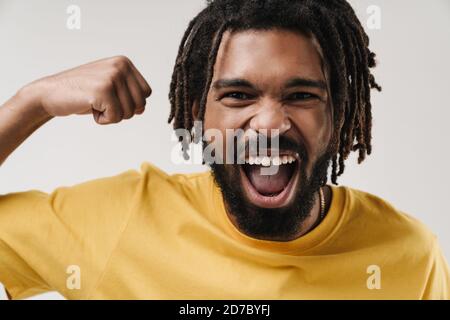 Image d'un homme africain criant et heureux qui se pose isolé arrière-plan de mur gris montrant le geste du gagnant Banque D'Images