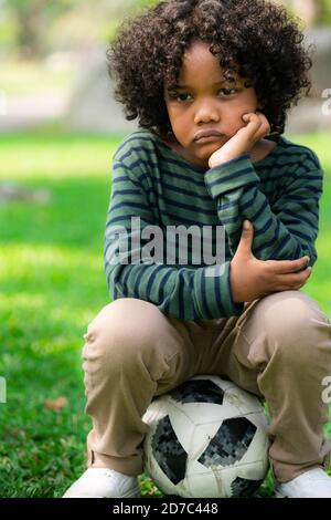 Peu ennuyé malheureux african american kid assis dans le parc. Le garçon montrant l'émotion négative. Le concept de l'enfant. Banque D'Images