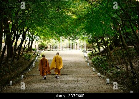 Deux moines marchant sur une route avec un tunnel vert. Vue arrière, jardin ombragé dans un temple à Kyoto Japon Banque D'Images