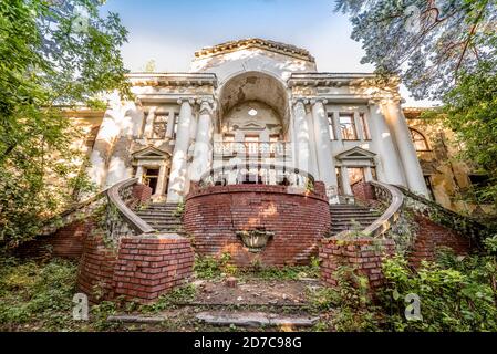 Bâtiment délabré abandonné dans le vieux parc. Escaliers, colonnes et balustrade. Seule la façade surcultivée de forêt est restée. Exemple de Banque D'Images