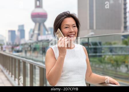 Téléphone Femme asiatique mature femme d'affaires chinoise d'âge moyen parlant affaires Sur un smartphone mobile, appelez à l'extérieur de Shanghai Street avec Pearl tour vers l'intérieur Banque D'Images