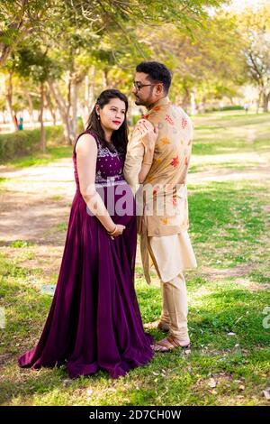 Jeune femme enceinte asiatique indienne avec son mari portant une tenue traditionnelle debout dans un parc ou un jardin pour écrire du texte. Banque D'Images