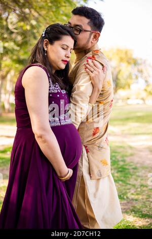 Jeune femme enceinte asiatique indienne avec son mari portant une tenue traditionnelle debout dans un parc ou un jardin pour écrire du texte. Banque D'Images