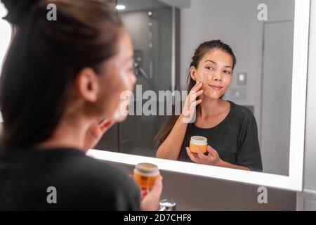Soins de la peau femme mettant masque de visage produit de nettoyage soin de la peau beauté Style de vie - femme asiatique regardant dans le miroir LED dans la salle de bains application de nettoyant pour le visage Banque D'Images