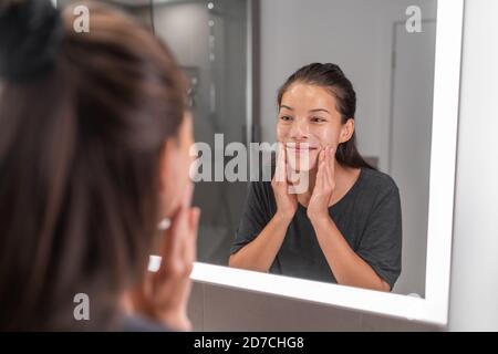 Femme se lavant le visage matin beauté soin de la peau routing heureux en utilisant la mousse de savon dans le miroir éclairé LED. Asie jeune fille massage visage exfoliate gommage Banque D'Images