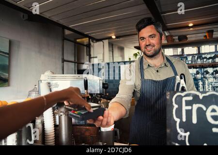 Serveur souriant recevant le paiement pour le café chaud de la part de la femme un café branché Banque D'Images