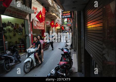 Famille de trois sur une moto dans une voie typique à Hanoi, Vietnam Banque D'Images