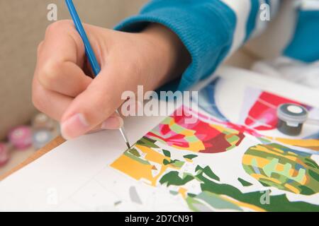 6 - gros plan multicolore de la peinture par nombres. La main jeune et brillante féminine contient le pinceau bleu vif avec des détails comme il peint vert Banque D'Images