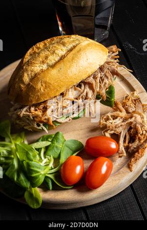 Sandwich avec de la viande tirée avec de la laitue et des tomates cerises sur la planche à découper. Banque D'Images