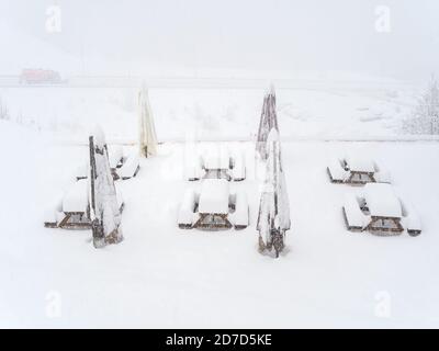 Des tables enneigées avec des bancs et des parasols d'extérieur pliés sont installés le site par une journée de neige brumeuse Banque D'Images