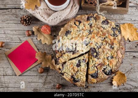 Cuisine d'automne confortable. Gâteau d'automne fait maison avec noix et prunes et carte en papier vide pour le texte sur fond en bois, vue du dessus, espace de copie. Banque D'Images