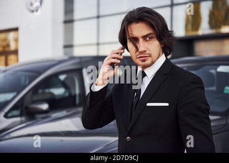 Portrait du beau jeune homme d'affaires en costume noir et cravate à l'extérieur près d'une voiture moderne Banque D'Images