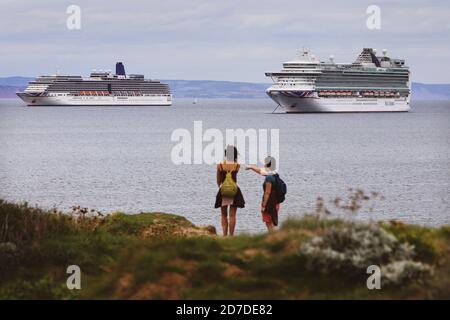 Un couple bénéficie d'une vue sur d'énormes navires de croisière ancrés au large de Torbay à Devon, au Royaume-Uni, dépourvus de passagers pendant la pandémie du coronavirus. Note: Les navires sont l'Azura et l'Arcadia. Tous deux exploités par P&O. Banque D'Images