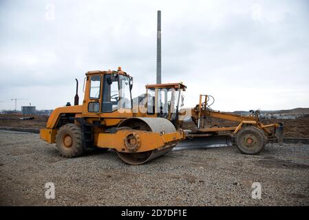 Niveleuse et compacteur de sol au niveau d'un chantier de construction le sol et les pierres de gravier pour la construction d'une nouvelle route asphaltée. Vibration unique Banque D'Images