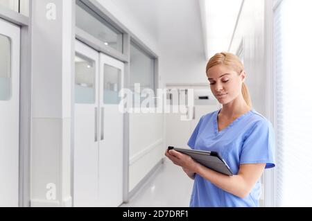 Femme médecin portant des exfoliants dans le couloir de l'hôpital à l'aide d'une tablette numérique Banque D'Images