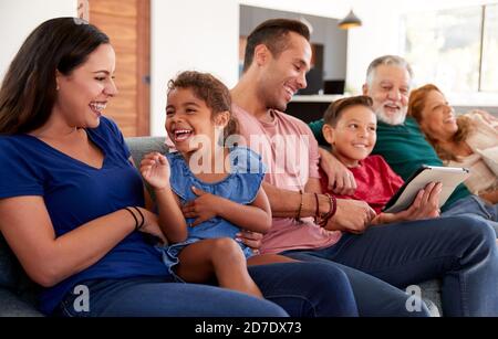 Famille hispanique de plusieurs générations se détendant sur le canapé pendant que le petit-fils joue avec Tablette numérique Banque D'Images