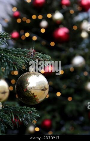 Boules de Noël dorées et rouges accrochées à des branches de sapin sur fond de lumières festives, prises verticales pour format mobile. Arbre du nouvel an avec décorations Banque D'Images