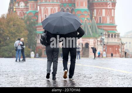 Pluie dans un Moscou, couple en vêtements d'automne avec un parapluie marchant sur la place Rouge sur fond de la cathédrale Saint-Basile. Personnes par temps pluvieux Banque D'Images