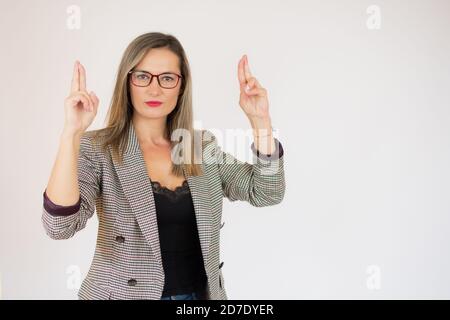 Jeune jolie femme qui croise avec inquiétude les deux doigts, se sentant inquiète et souhaitant ou espérant bonne chance contre le mur blanc Banque D'Images