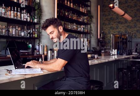 Homme propriétaire du bar-restaurant assis au comptoir travaillant sur Ordinateur portable Banque D'Images