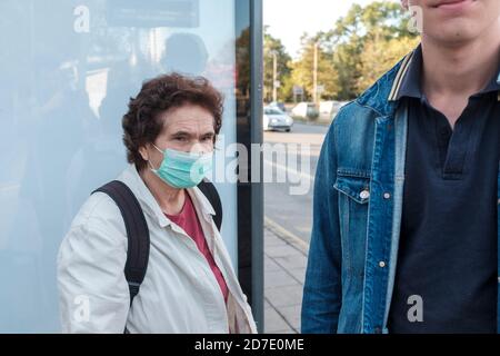Covid 19 ans femme portant un masque de protection près de jeune homme sans masque à l'arrêt de bus Banque D'Images