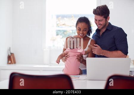 Famille avec bébé fille dans la cuisine utilisant un ordinateur portable sur le comptoir Banque D'Images