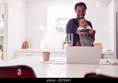 Père avec bébé fille en Sling Multi-tâches travailler à la maison Sur ordinateur portable Banque D'Images