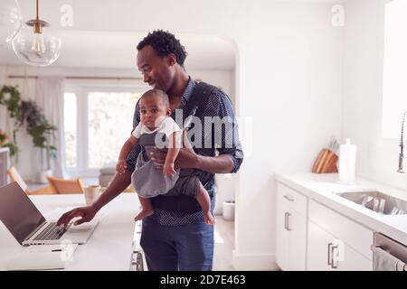 Père avec bébé fille en Sling Multi-tâches travailler à la maison Sur ordinateur portable Banque D'Images