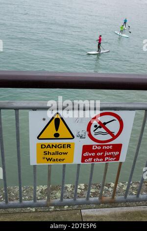 Un instructeur de paddle-board dans un haut orange donne une leçon à deux enfants dans la mer calme à l'ouest de Boscombe Pier à Bournemouth lors d'une journée de février terne. 10 février 2015. Photo: Neil Turner Banque D'Images