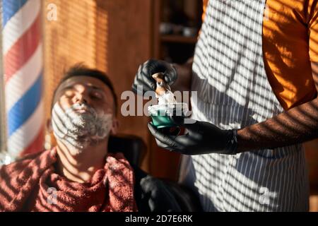 Coiffeur en gants stériles préparant la crème à raser dans un salon de coiffure Banque D'Images