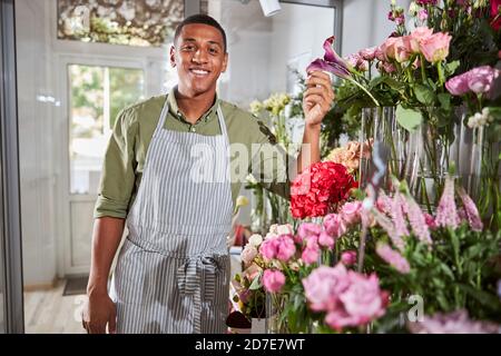 Joyeux assistant de magasin de fleurs donnant une touche à une fleur Banque D'Images