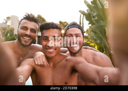 Trois amis masculins à la fête de piscine d'été prenant Selfie sur Téléphone portable Banque D'Images