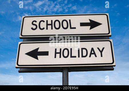 École vs vacances. Deux panneaux de signalisation blancs avec flèche sur poteau métallique avec mot. Route directionnelle. Panneau Crossroads Road, deux flèches. Fond bleu ciel. Banque D'Images